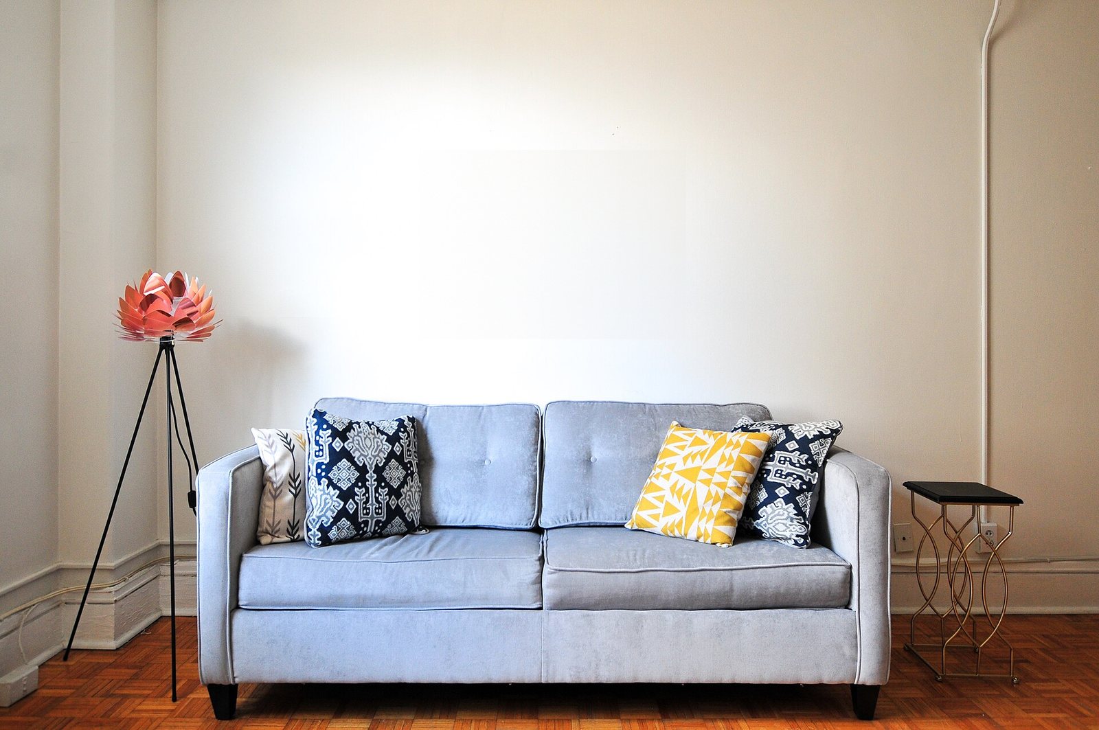 A living room with a grey sofa against a plain wall and a wood floor.